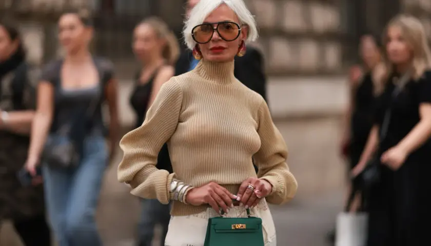 Elegancka kobieta z siwymi włosami i okularami w stylu retro, trzymająca zieloną torebkę. Jej styl pokazuje, że pewne rzeczy nigdy nie są passe.