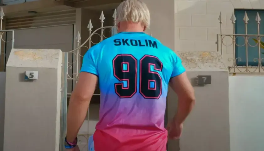 Mężczyzna w koszulce z napisem SKOLIM i numerem 96, stojący przed domem z numerem 5.