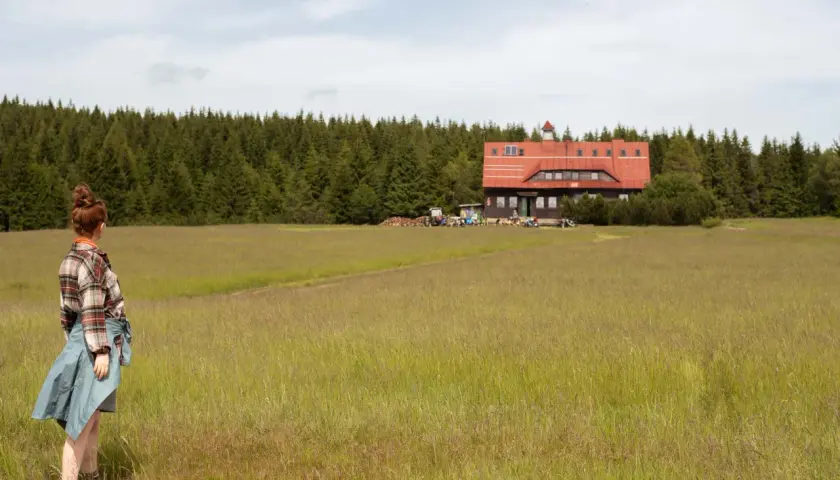 Dziewczyna w kratę podziwia schronisko na tle lasu w Górach Izerskich, Polska.