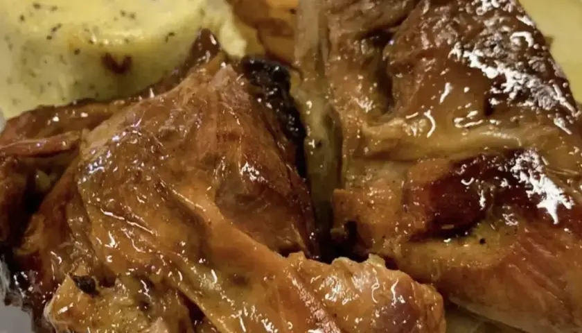 Succulento agnello al forno, dorato e lucido, servito con patate arrosto e una cremosa salsa verde.