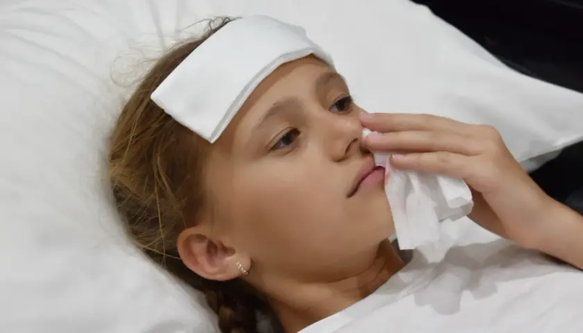 Bambina con impacco sulla fronte e fazzoletto per fermare il sangue dal naso.