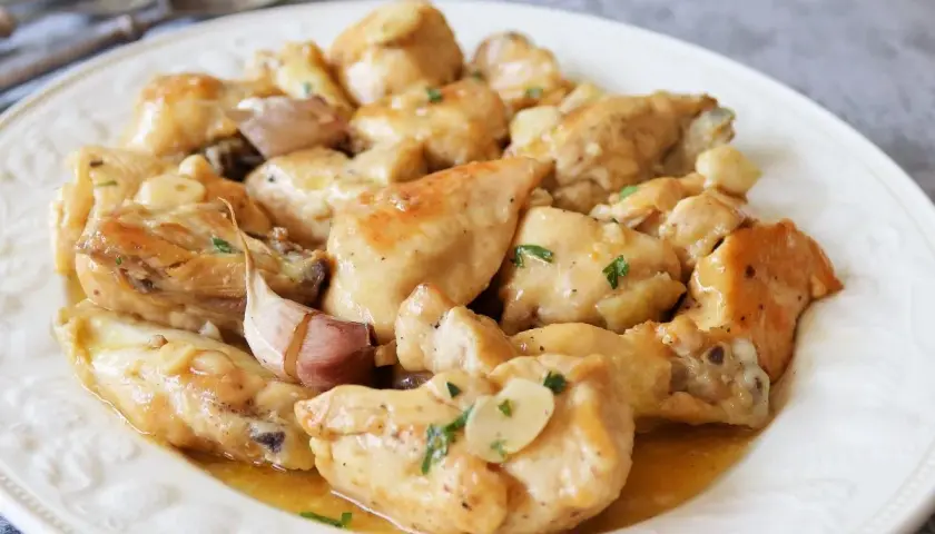 Sabroso pollo al ajillo servido en un plato blanco, con trozos de pollo dorados y jugosos, cubiertos con una salsa de ajo y perejil.