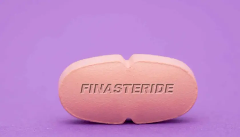 Różowa tabletka z napisem FINASTERIDE na fioletowym tle.