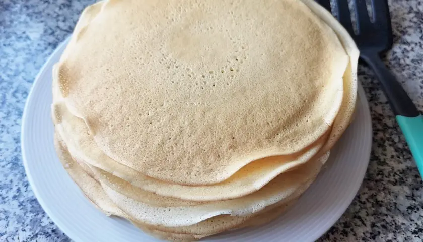 Stos cienkich, złotych placków, idealne ciasto na krokiety, leży na białym talerzu obok łopatki.