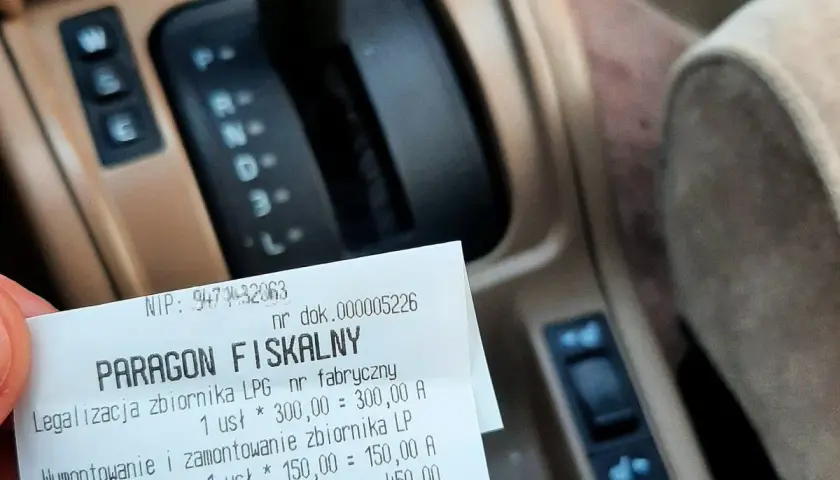 Paragon fiskalny za legalizację i montaż zbiornika LPG na tle deski rozdzielczej samochodu.
