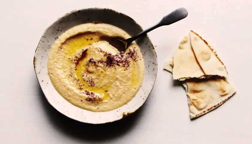 Un bol de houmous onctueux, arrosé d'huile d'olive et saupoudré d'épices, prêt à être dégusté avec du pain pita. Une recette houmous simple et savoureuse.