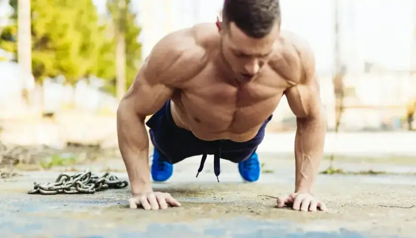 Mięśniowy mężczyzna wykonuje pompki na biceps, z łańcuchem obok.