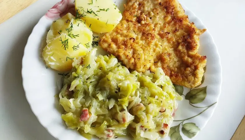 Młoda kapusta zasmażana z boczkiem, podana z ziemniakami i kotletem. Pyszny, domowy obiad.