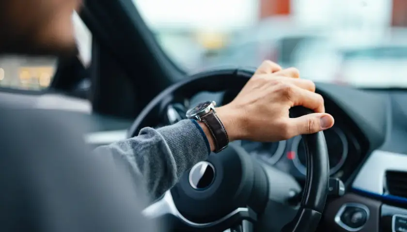 Mano en el volante, reloj de pulsera, tablero de coche. El conductor nota un fallo en la dirección asistida.