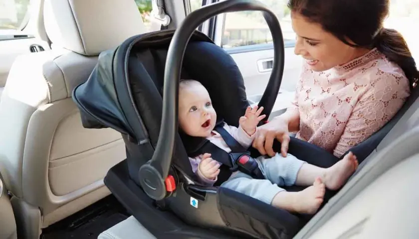 Mama z uśmiechem obserwuje dziecko w foteliku samochodowym. To jeden z rodzajów fotelików samochodowych, zapewniający bezpieczeństwo najmłodszych.