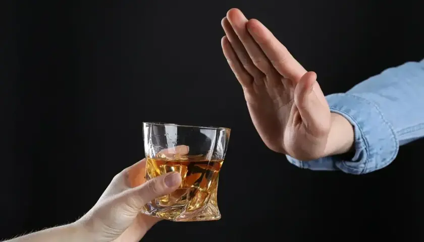 Ręka odrzuca szklankę z bursztynowym płynem. Czy dzień przed wizytą u dentysty można pić alkohol? Lepiej nie ryzykować.