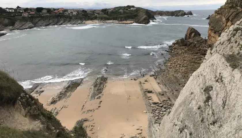 Vista panorámica de la playa San Juan de la Canal, con formaciones rocosas y casas en la costa.