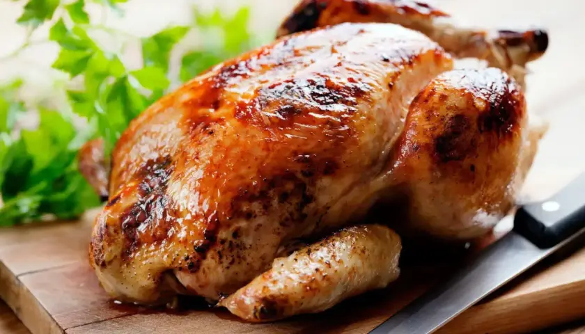 Un délicieux poulet rôti doré sur une planche en bois, prêt à être dégusté. Quel vin avec poulet rôti ? Un blanc fruité ou un rouge léger serait parfait.