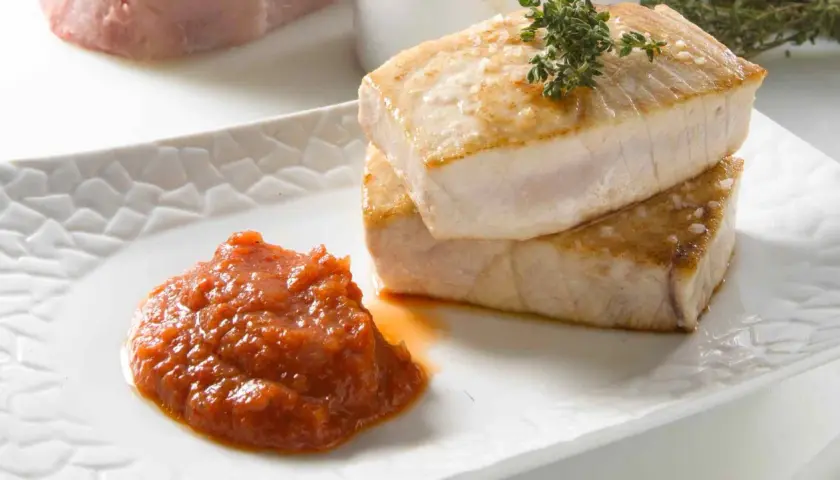 Dos jugosos medallones de atún a la plancha, con sal gruesa y romero, acompañados de una cucharada de salsa de tomate casera.