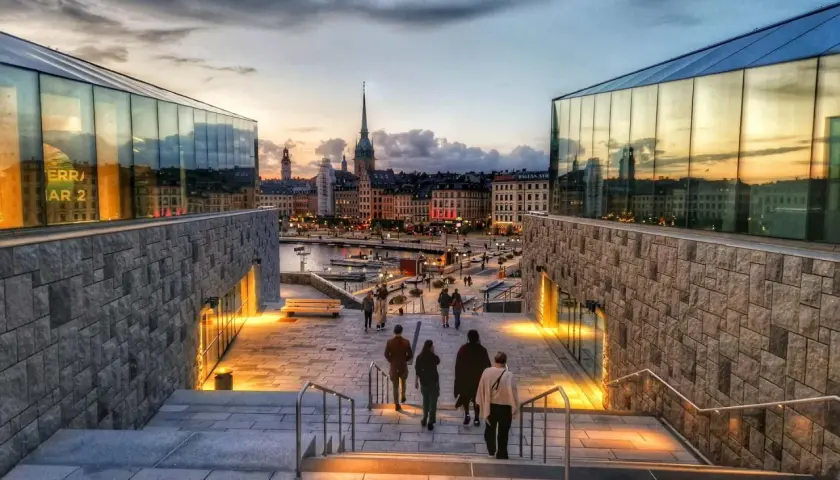 En vacker stadsvandring i Stockholm vid skymningen. Folk promenerar nerför trappor mot en upplyst stadssilhuett med vattnet i förgrunden.