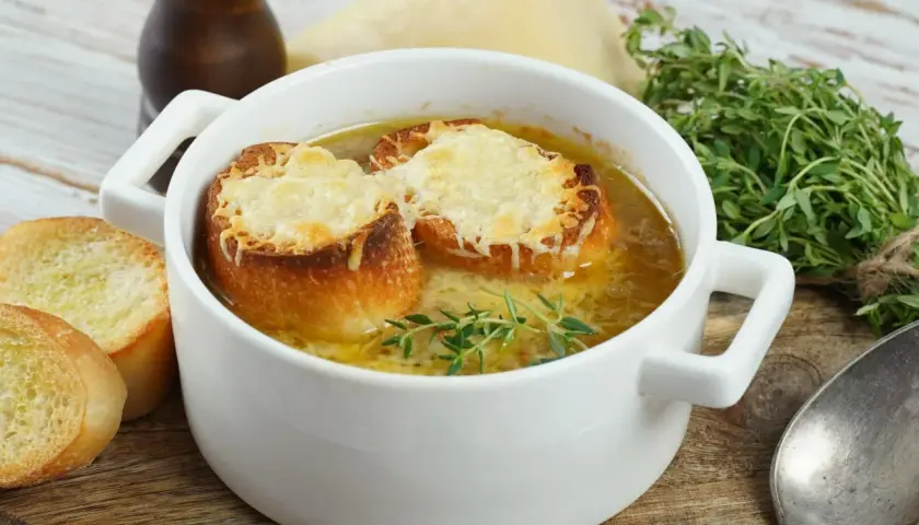 Aksamitna zupa cebulowa przepis, podana w białej miseczce z grzankami zapieczonymi z serem i gałązką tymianku.