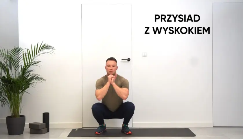 Mężczyzna w pozycji do przysiadów z wyskokiem, gotowy do ćwiczeń.