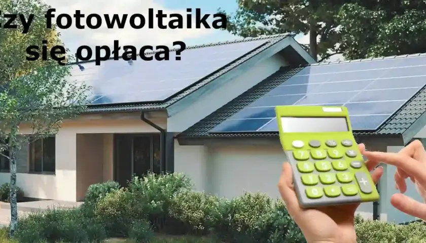 Dwie ręce trzymają kalkulator obok domu z panelami fotowoltaicznymi na dachu. Czy fotowoltaika się opłaca?