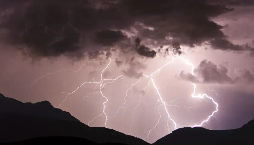 Gewitter in den Bergen: Blitze zucken durch dunkle Wolken über silhouettierten Gipfeln.