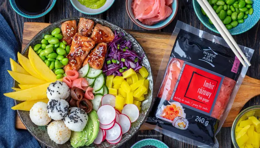 Kolorowy bowl z lososiem, ryżem, mango, awokado, edamame i marynowanym imbirem. Obok opakowanie imbiru różowego.