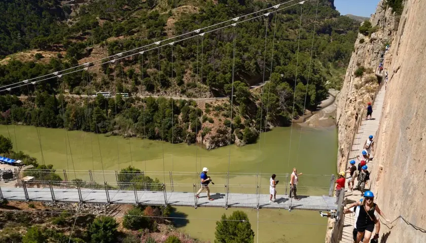 Visitantes caminan por la pasarela del Caminito del Rey, una impresionante ruta del rey entre acantilados y un río verde.