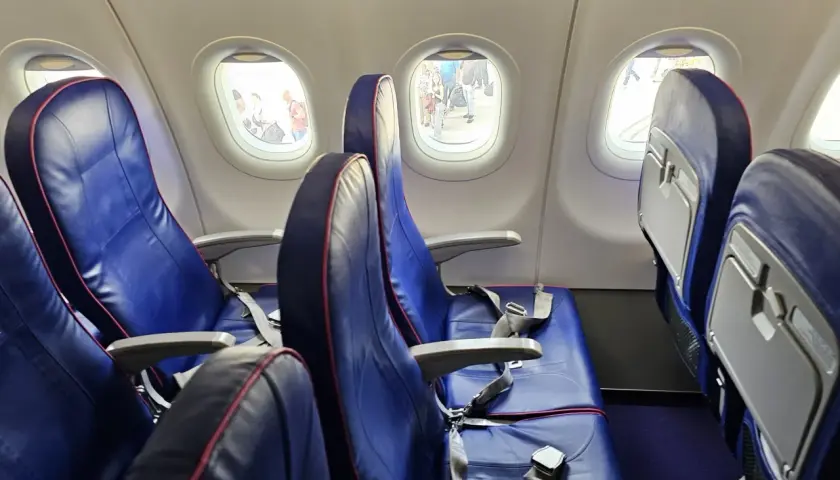 Puste siedzenia w samolocie Wizzair, przez okna widać ludzi na płycie lotniska. Automatyczna odprawa Wizzair przebiegła sprawnie.