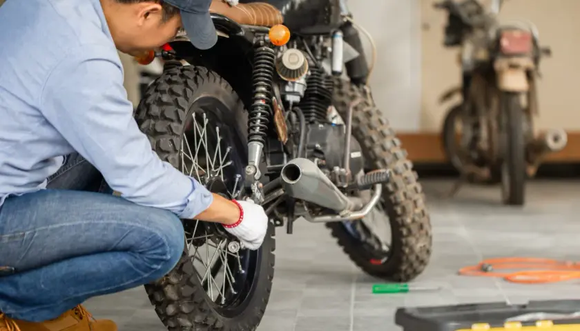 Mecánico revisa moto para su homologación. Herramientas y otra moto en el fondo.