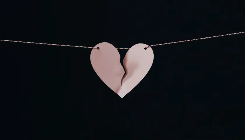 Un cuore di carta rosa, spezzato a metà, pende da un filo. Simbolo di un amore non corrisposto.