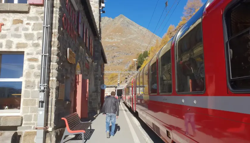 En man går längs en tågstation i bergen, redo för sin tågluffa Europa rutt. En röd tågvagn står parkerad.