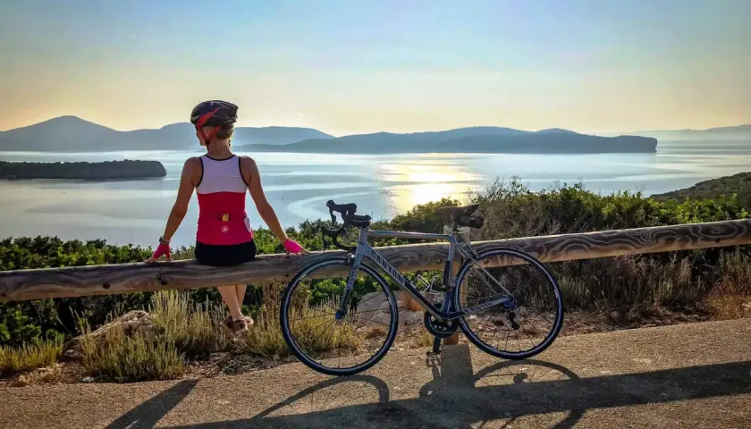 Ciclista descansa tras un tour en bicicleta en Cerdeña, disfrutando de la vista al mar al atardecer.