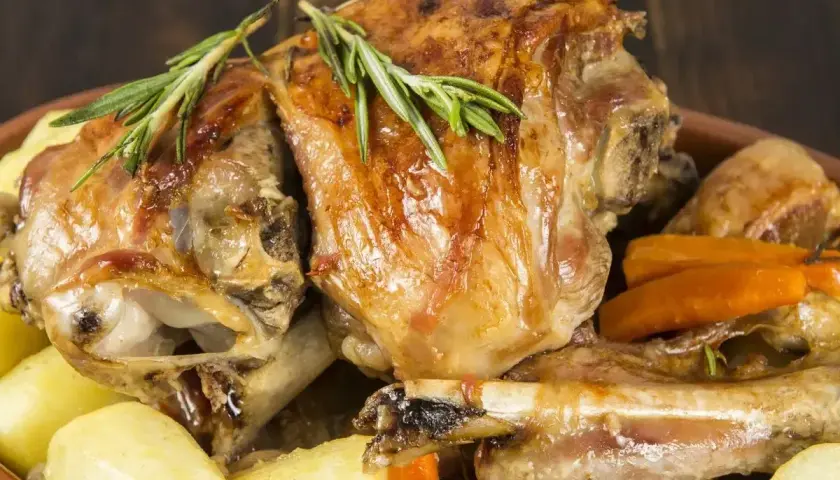 Pyszne dania z baraniny: pieczone kawałki mięsa z ziemniakami i marchewką, ozdobione rozmarynem.