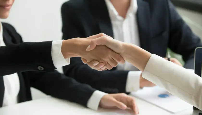 Dwie osoby w garniturach ściskają sobie dłonie, symbolizując udaną współpracę. To właśnie jest trade marketing co to znaczy - budowanie relacji biznesowych.