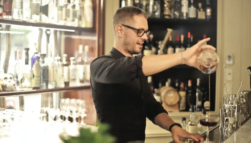 Barman w okularach nalewa drinka. Zastanawiasz się, ile się zarabia jako barman? To zależy od lokalu i doświadczenia.
