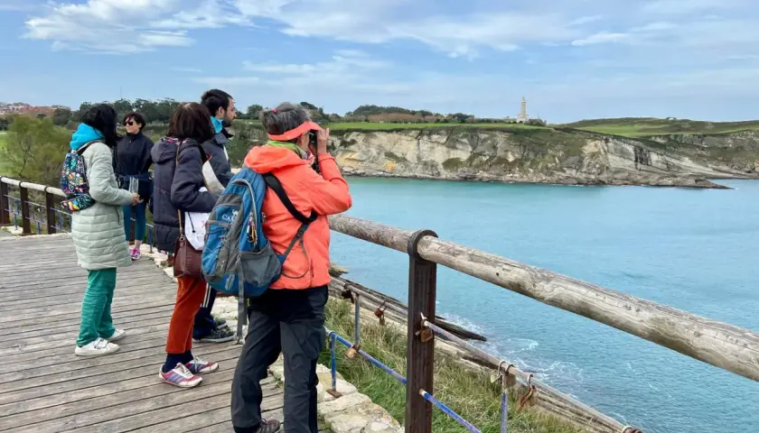 Disfrutando de las rutas por Santander, un grupo de amigos admira el faro y la costa desde un mirador de madera.