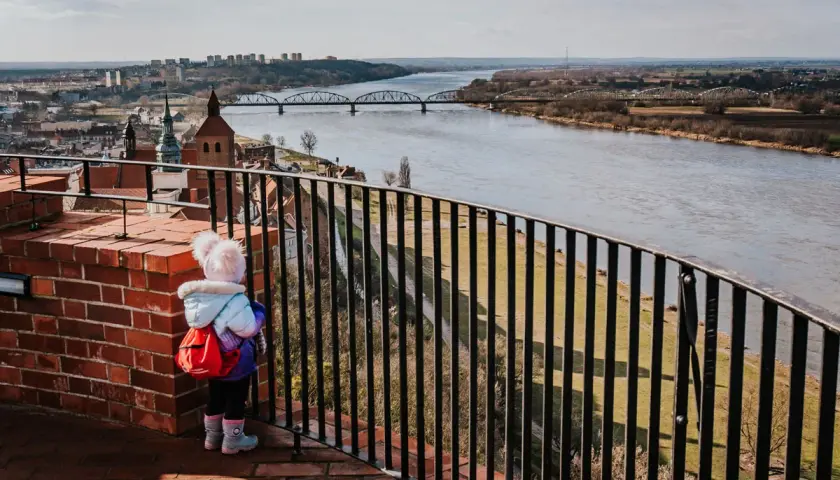 Dziecko z plecaczkiem podziwia panoramę Grudziądza i Wisły. Widok na mosty i miasto to jedne z głównych atrakcji.