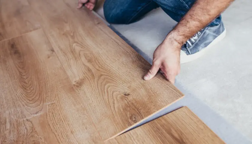 Installazione di un nuovo pavimento in laminare parquet. Le assi in legno chiaro vengono posate con cura.