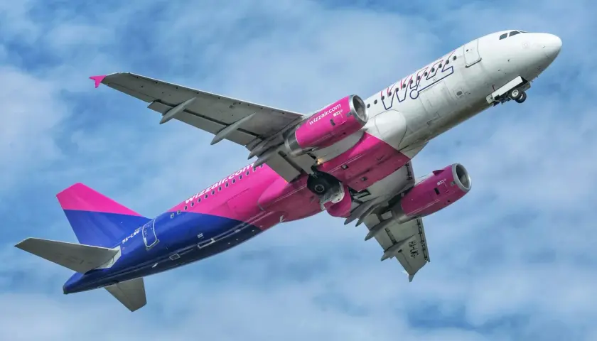 Samolot Wizz Air z różowo-niebieskim ogonem wznosi się na tle błękitnego nieba.