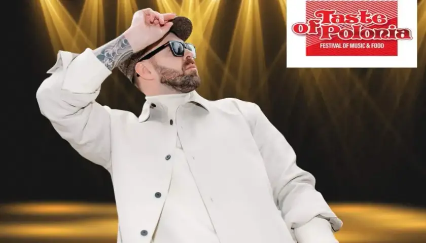 Grzegorz Hyży wstaje na scenie Taste of Polonia, w białej kurtce i czapce, w blasku reflektorów.