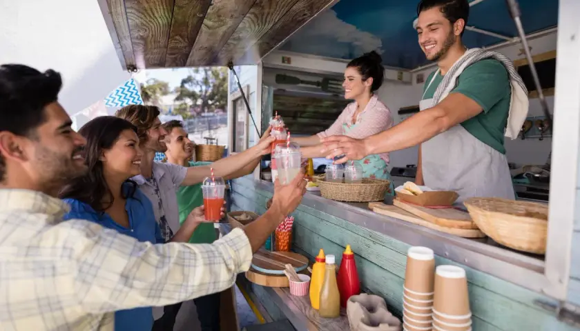 Uśmiechnięci klienci odbierają napoje od barmana w food trucku. Ciekawe, ile zarabia barman za noc przy takiej popularności!