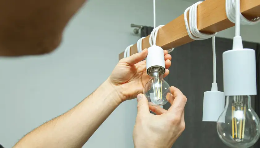 Ręce wkręcają żarówkę LED do oprawy. Czy 15w led ile to wat? To energooszczędne oświetlenie.
