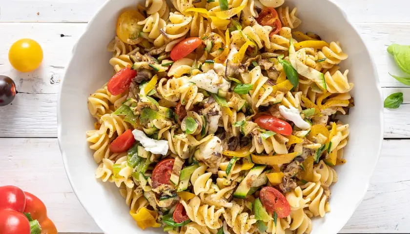 Un piatto invitante di pasta fredda saporita con fusilli, pomodorini, zucchine, peperoni gialli e mozzarella.