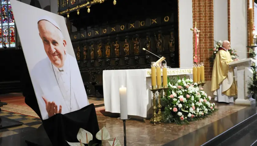 Papieski pontyfikat upamiętniony portretem i kwiatami w kościele.