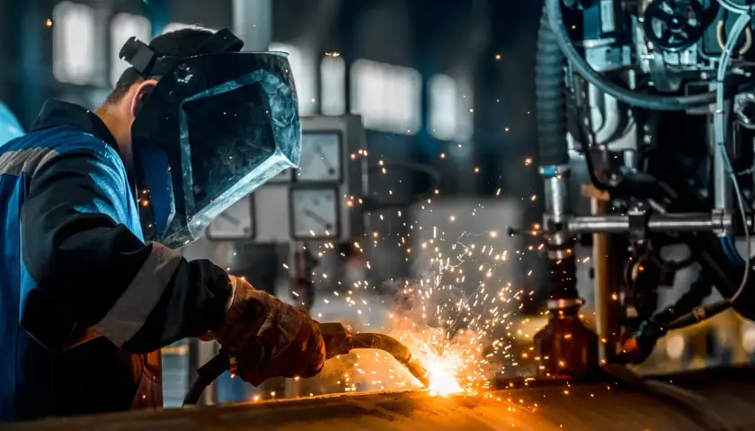Spawacz w masce ochronnej używa elektrod do aluminium, tworząc iskry podczas pracy przy metalowej konstrukcji.
