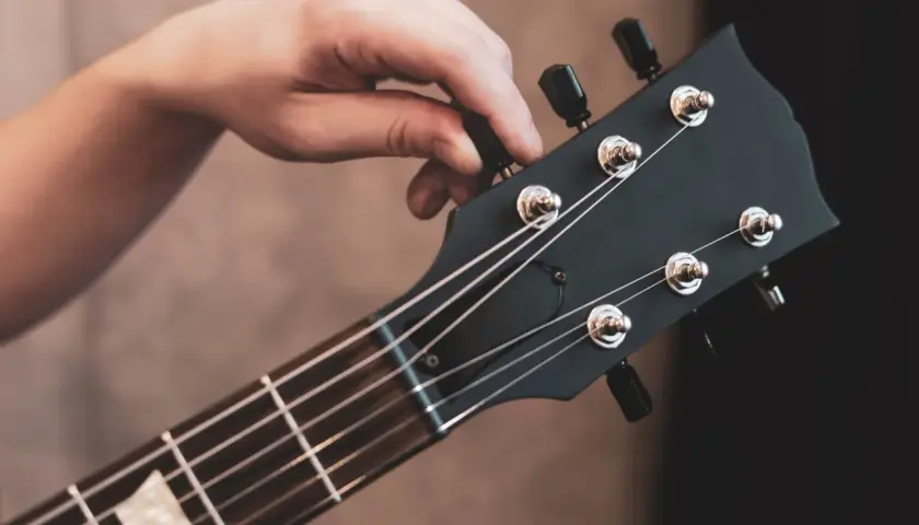 Dłoń kręci kluczem przy główce gitary elektrycznej, pokazując jak nastroić gitarę elektryczną bez stroika, słuchając dźwięku.