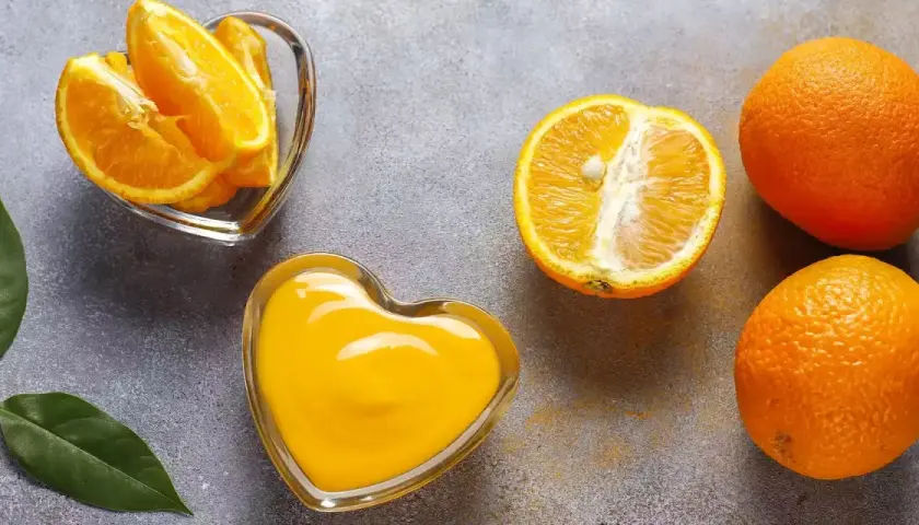 Arance fresche, spicchi e succo in ciotole a forma di cuore. Scopri quale alimento contiene più vitamina C per un cuore sano!