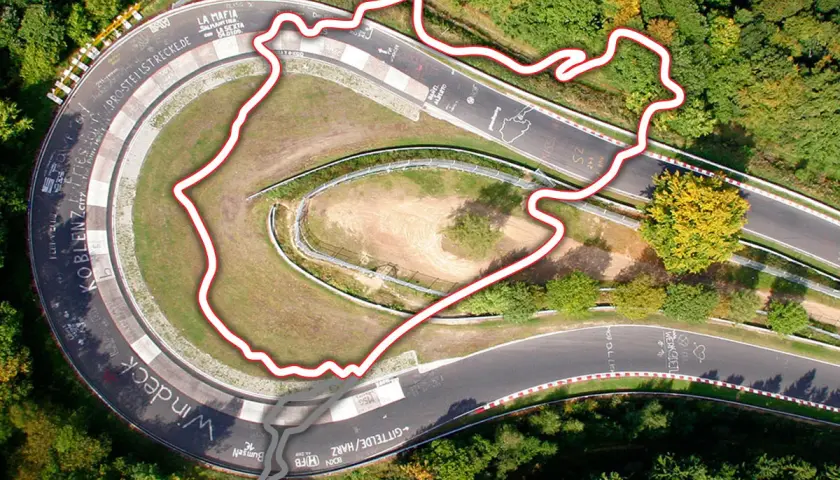 Widok z lotu ptaka na fragment toru Nürburgring otoczony lasem. Czerwona linia obrysowuje trasę, ukazując jej kręty kształt.