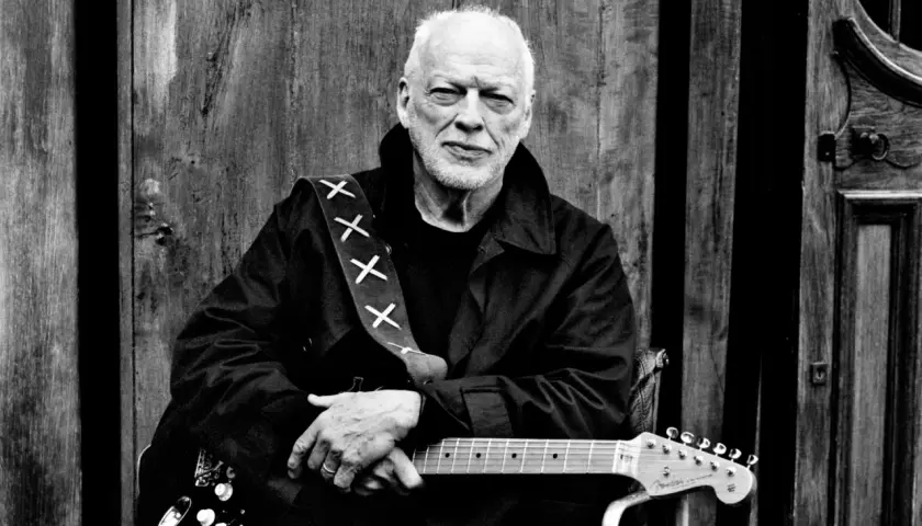 David Gilmour z najdroższą gitarą na świecie, oparty o drewniane drzwi.