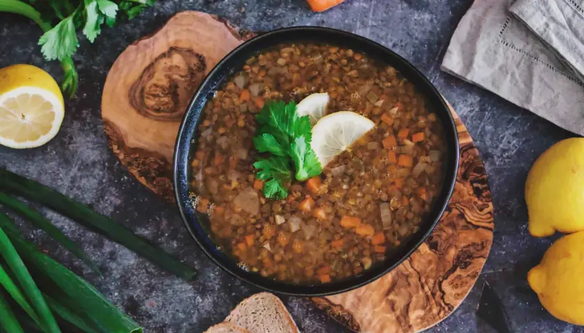 Herzhafte italienische Linsensuppe mit Karotten und Sellerie, garniert mit Zitrone und Petersilie, daneben Brot und frische Kräuter.