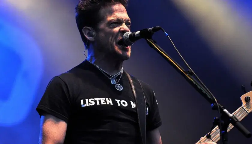 Jason Newsted z zespołu, w czarnej koszulce z napisem "LISTEN TO N", śpiewa do mikrofonu, grając na basie.