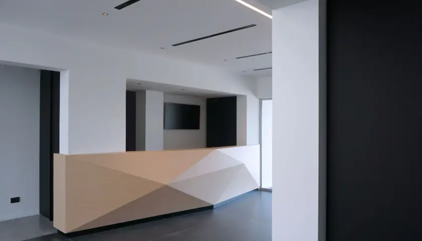Moderno bancone reception in cartongesso con pannelli geometrici in legno chiaro.